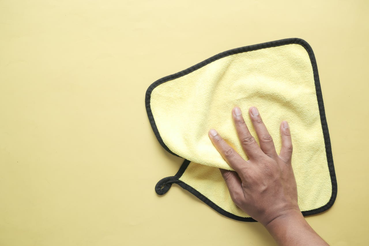 hero-img A hand using a microfiber cloth to wipe a yellow background, demonstrating cleaning and hygiene concepts.