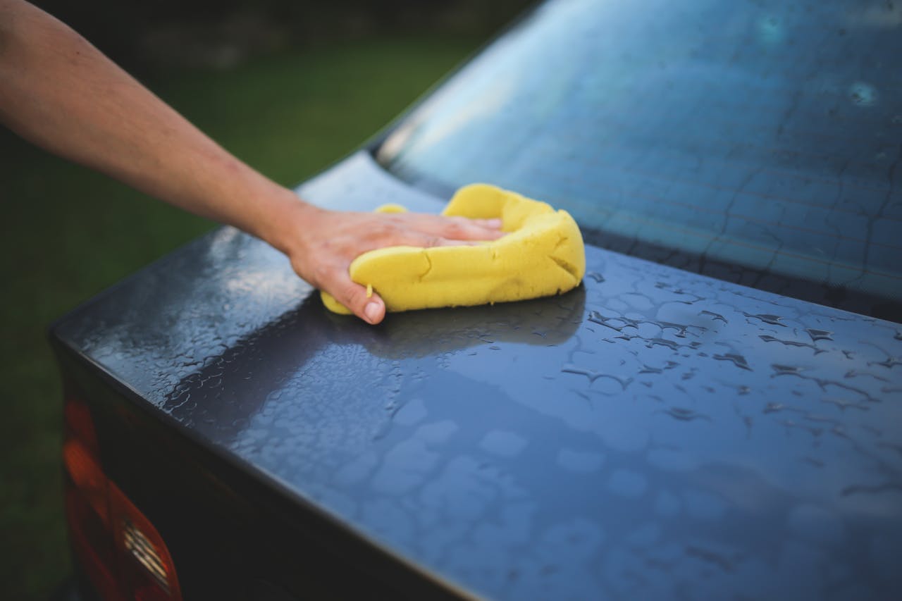 about-01 Hand cleaning car with a yellow sponge, showcasing car detailing and washing process.