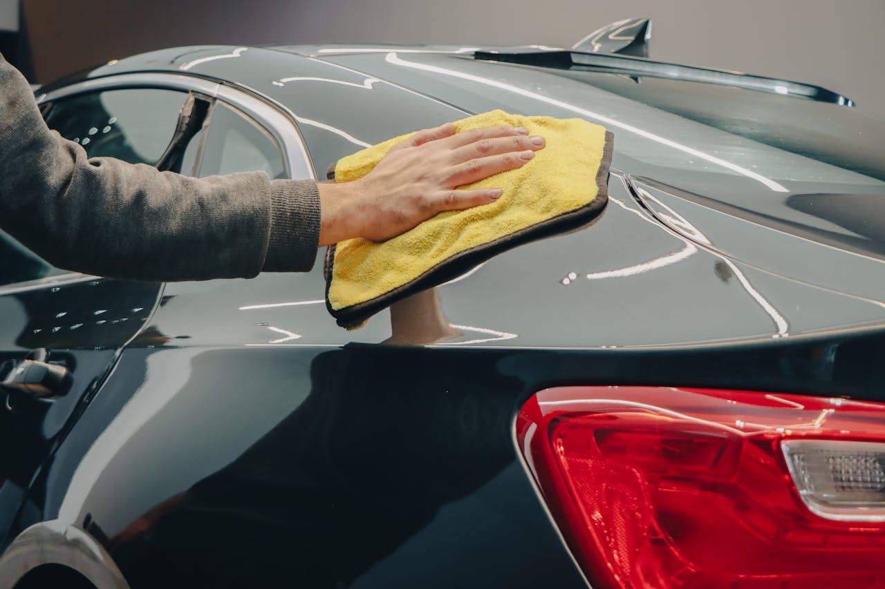services-01 Close-up of hand polishing a shiny car with a yellow cloth indoors.
