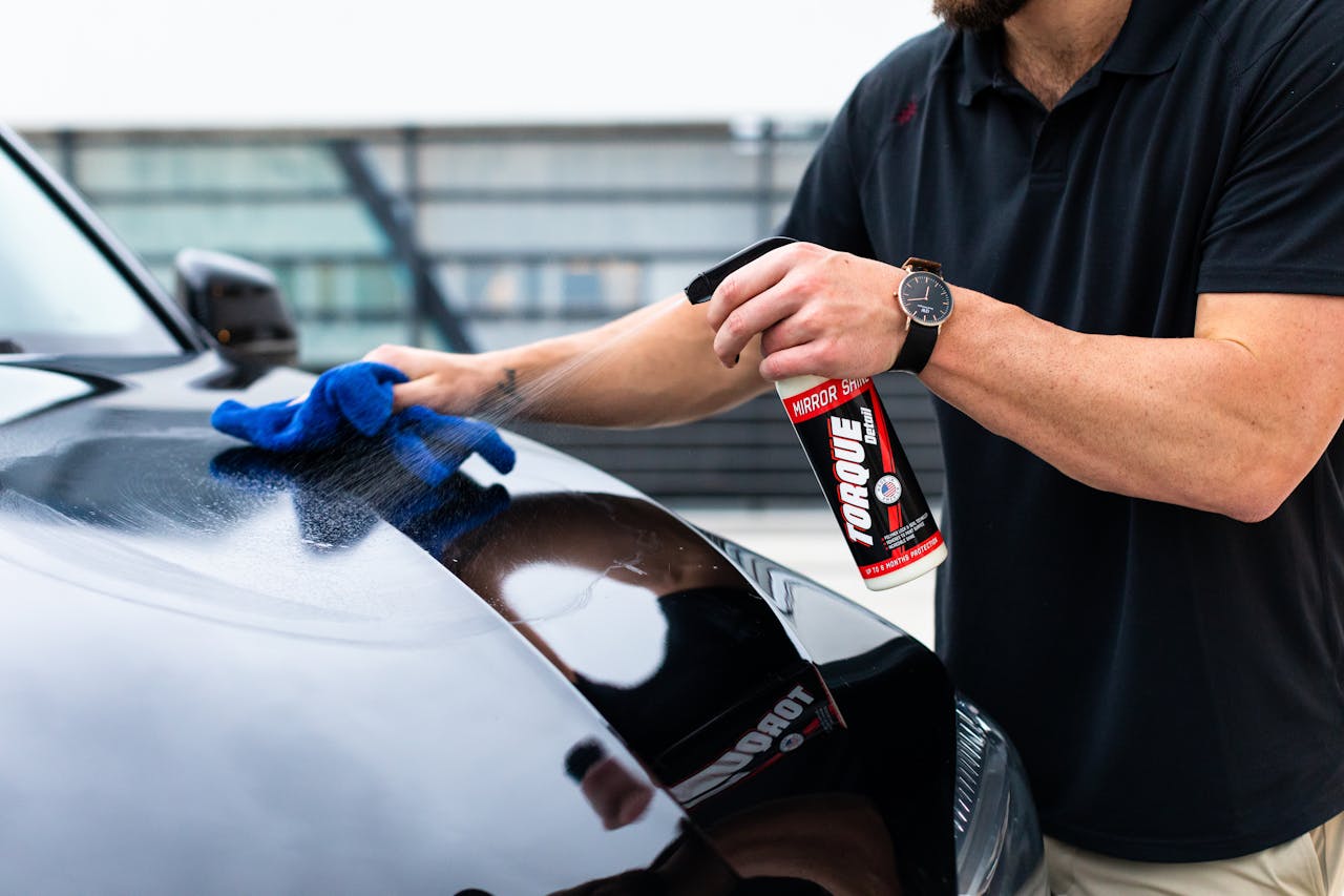 services-02 A man cleaning a black car hood with a spray and microfiber cloth.